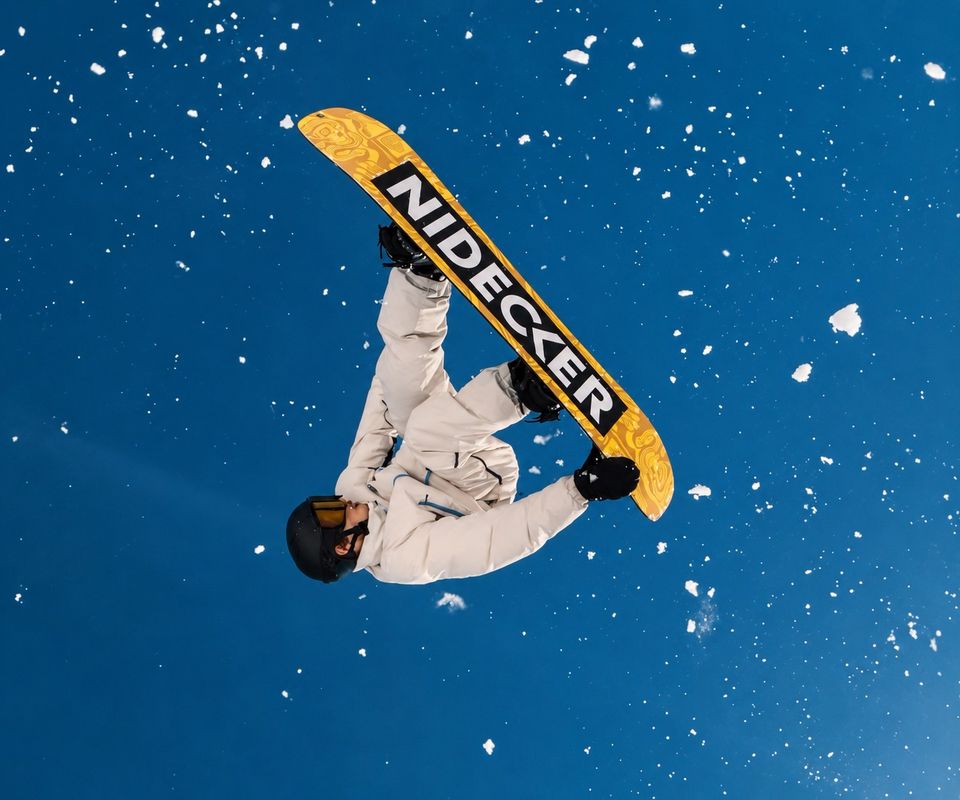 Corentin en l'air, grab sur sa board Nidecker sous un ciel bleu